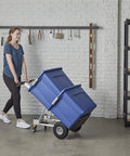 Person using ✝️ COSCO 4-in-1 Folding Series Hand Truck with Flat-Free Wheels carrying a large blue container in a garage.