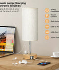 Bedside Table Lamp With 3 Way Dimmable Touch Control, USB C Charging Ports And AC Outlet on wooden desk with devices charging
