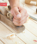 Hand using a plane to smooth wood surface with Nelson Wood Shims logo, relating to Versatile 8 Inch Wood Shims Set For DIY Projects And Home Improvement By Nelson, 24 Pack Delivers Easy Leveling And Spacing For Cabinets, Doors, Floors, Tables, Appliances, Stairs, And More, Trusted For Quality And Longevity.