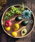 Top view of 16 Inch Lazy Susan Turntable With Handles Wooden Rotating Tray With Raised Rim displaying fruits and flowers.