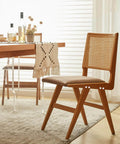 Wooden dining chair with woven backrest next to a table with a fringed cloth in a sunlit dining room.