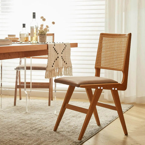 Wooden dining chair with woven backrest next to a table with a fringed cloth in a sunlit dining room.