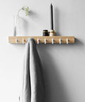 Wall-mounted shelf with hooks holding a candle, vase with flower, and gray towel