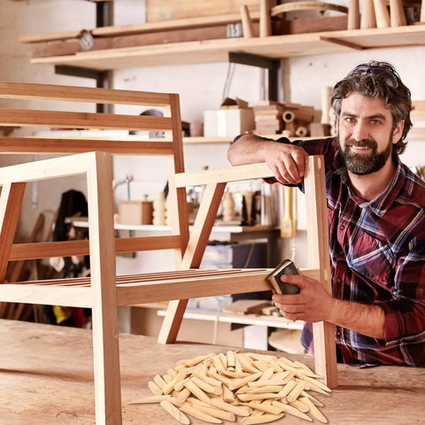 Carpenter using solid pine pocket hole plugs on wooden furniture in workshop, Premium Solid Pine Pocket Hole Plugs Pack Of One Hundred Twenty Pieces Three Eighth Inch Diameter For Screw Holes And Pocket Hole Jigs Woodworking For Diyers And Pros With A Smooth Conical Design For A Clean Seamless And Durable Finish visible in foreground.