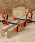 Two Pack Six Inch One Hand Clamp And Spreader Set With 300 Lb Clamping Force holding wooden planks on a workbench