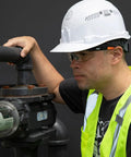 Man wearing Low Profile Safety Glasses Narrow Lens Z87 1 Anti Fog Scratch Resistant 2 Pack, hard hat, and safety vest working with machinery.