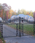 Elegant black wrought iron driveway gate with autumn trees, showcasing an upscale home in the background.