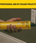 Person holding yellow caulk gun cartridge, labeled for professional and DIY sealing projects, near a wall outlet.