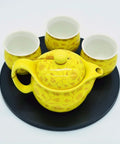 Yellow teapot and cups on black turntable platform.