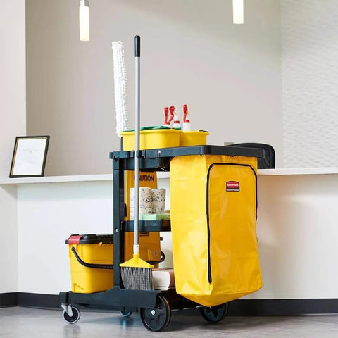 Heavy Duty 24 Gallon Front Zippered Vinyl Replacement Bag For Industrial Janitorial Carts Yellow Waste Linen And Trash Collection Durable Front Loading Bag For Commercial Cleaning Compatible With Rubbermaid Commercial Carts attached to a black cart alongside mops and other cleaning supplies in an office setting.