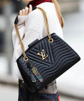 Person holding a designer black handbag with gold chain straps and colorful tag, wearing a white sweater and jeans.