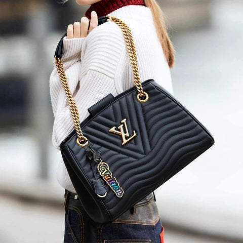 Person holding a designer black handbag with gold chain straps and colorful tag, wearing a white sweater and jeans.